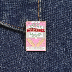 Broche en émail carte de Tarot rose avec livre et mains sur fond denim