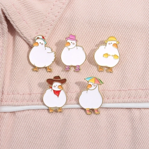 Close-up of five cute cartoon duck enamel pins with colorful hats on pink denim