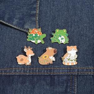 Detail view of five cute animal enamel pins including a frog and capybara on denim fabric