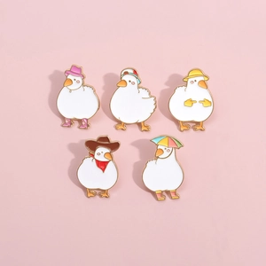 Set of 5 cute white duck enamel pins with various hats on a soft pink background