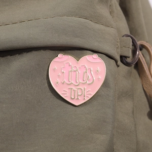 Vue détaillée du pin's cœur en émail rose avec texte tits UP! sur un sac en toile
