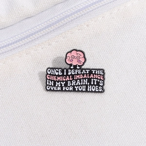 Detail of cartoon pink brain enamel pin with funny quote on black metal badge