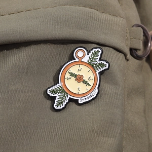 Détail d'une broche boussole en émail avec fleur orange sur sac en toile verte