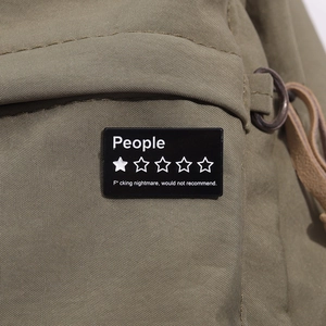 Détail d'un pin's émaillé noir minimaliste avec une étoile fixé sur un sac vert