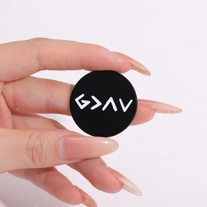 Macro detail of a round black metal badge with white geometric G > ^ v symbols held by hand