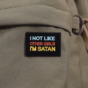 Dettaglio di spilla smaltata con testo I'M SATAN su borsa in nylon verde, vista ravvicinata
