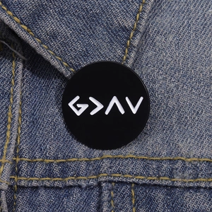 Detailed close-up of a black enamel 'God is Greater' pin on blue denim fabric