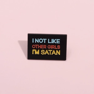 Dettaglio di una spilla smaltata rettangolare con testo colorato I AM SATAN su rosa