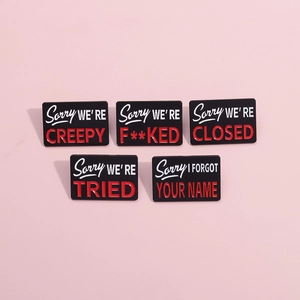 Close-up of black and red enamel metal pins with humorous slogans on a pink background