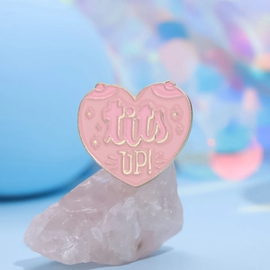 Broche en émail cœur rose avec lettrage tits UP! et bordure dorée sur une pierre