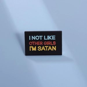 Close-up of black enamel pin featuring colorful text I'M NOT LIKE OTHER GIRLS I'M SATAN