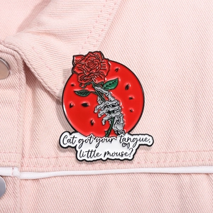 Macro shot of gothic red enamel rose brooch with skeleton hand on pink denim fabric