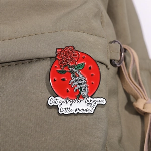 Detail view of skeleton hand holding a red rose enamel pin on a khaki canvas backpack