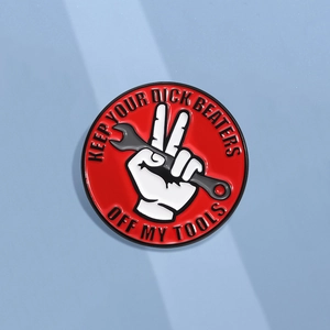 Detail of red enamel badge featuring a white hand holding a wrench with humorous text