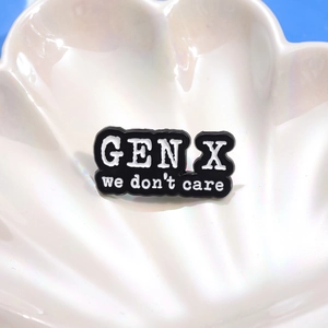 Minimalist Gen X We Don't Care black enamel pin badge on a decorative shell plate