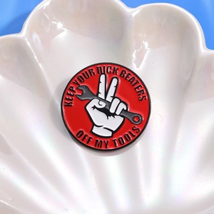 Red circular enamel pin featuring white hands with wrench and Keep Your Dick Beaters Off My Tools