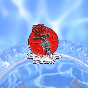 Detail of gothic enamel pin showing skeleton hand holding a red rose with moon