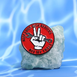 Macro detail of red enamel pin with tools warning text and finger gesture
