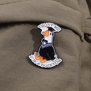 Close-up of Trust Me I'm a Ducktor enamel pin on an olive green canvas bag