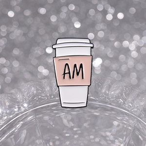 Detail of AM PM coffee cup enamel pin with pink sleeve on a stylish bokeh background