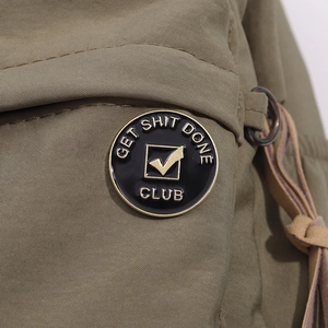 Detailed macro view of black enamel Get Shit Done Club badge on olive green canvas fabric