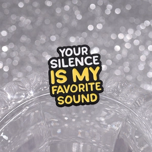 Dettaglio della spilla smaltata con testo YOUR SILENCE IS MY FAVORITE SOUND su fondo nero