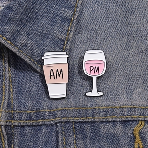Detailansicht der AM-Kaffee- und PM-Wein-Emaille-Pins auf blauem Denim-Stoff