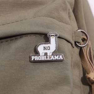 Cool white llama enamel pin with sunglasses and No Probllama text on green backpack