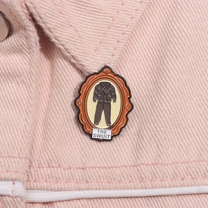 Detailed close-up of retro enamel frame brooch with THE SWUIT text on pink denim fabric