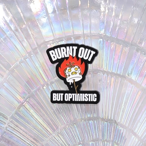 Macro shot of 'Burnt Out But Optimistic' enamel pin with marshmallow and flame detail