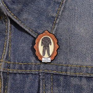 Close-up of vintage orange frame enamel pin with THE SWUIT text on denim jacket