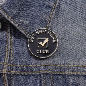 Detail of Get Shit Done Club enamel pin badge on a denim jacket collar close-up