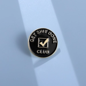 Close-up of black and gold Get Shit Done Club metal badge on light blue background
