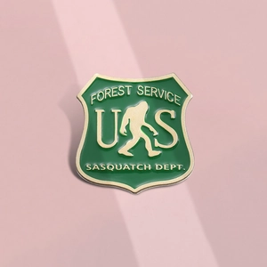 Detail of green and gold enamel shield badge featuring Sasquatch Forest Service design