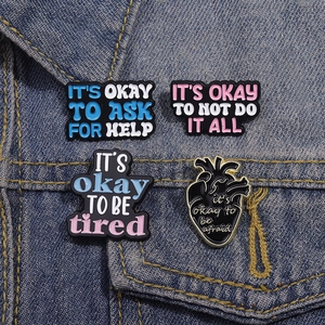 Detail von vier Emaille-Pins zur psychischen Gesundheit auf einer Jeansjacke mit Text