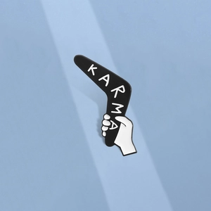 Close-up of black and white Karma boomerang enamel pin with hand on light blue background