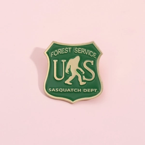 Detail of shield-shaped Forest Service Sasquatch Dept enamel pin with green finish