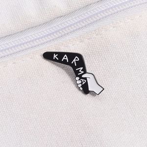 Detail of KARMA enamel pin with boomerang design pinned on white canvas bag fabric