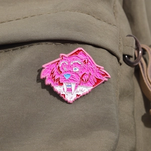 Spilla smaltata mostro rosa su borsa di tela verde, distintivo di bestia dai denti a sciabola
