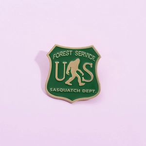 Green enamel Sasquatch Dept. Forest Service badge pin with gold trim and Big Foot silhouette