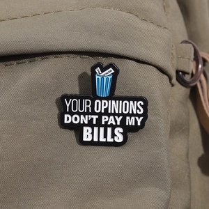 Détail d'une broche en émail sur sac en toile avec le texte Your Opinions Don't Pay My Bills
