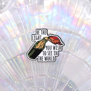 Enamel pin featuring a burning glass bottle with Be the Light inspirational quote