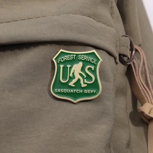 Macro detail of a green shield-shaped metal enamel pin with Sasquatch Dept engraving