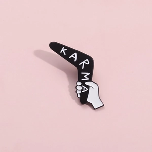 Macro detail of Karma boomerang enamel pin with hand design on pink background