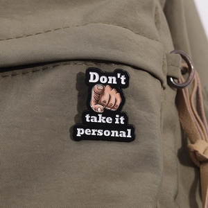 Macro shot of Don't Take It Personal enamel pin on dark green canvas jacket