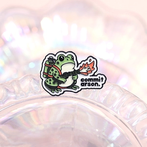 Whimsical green frog enamel pin holding a flamethrower and commit arson text
