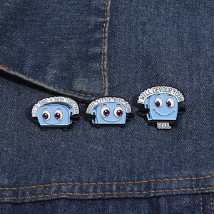 Funny blue toaster enamel pins with quirky text on dark denim jacket fabric