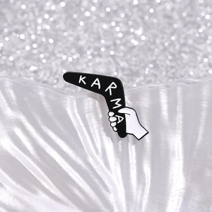 Macro shot of black enamel KARMA boomerang brooch with hand design and silver sparkle backdrop