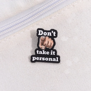 Detail of enamel pin with hand gesture and Don't take it personal text on canvas