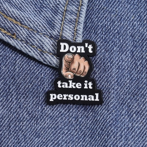 Detail of a black enamel pin with 'Don't take it personal' text on blue denim fabric